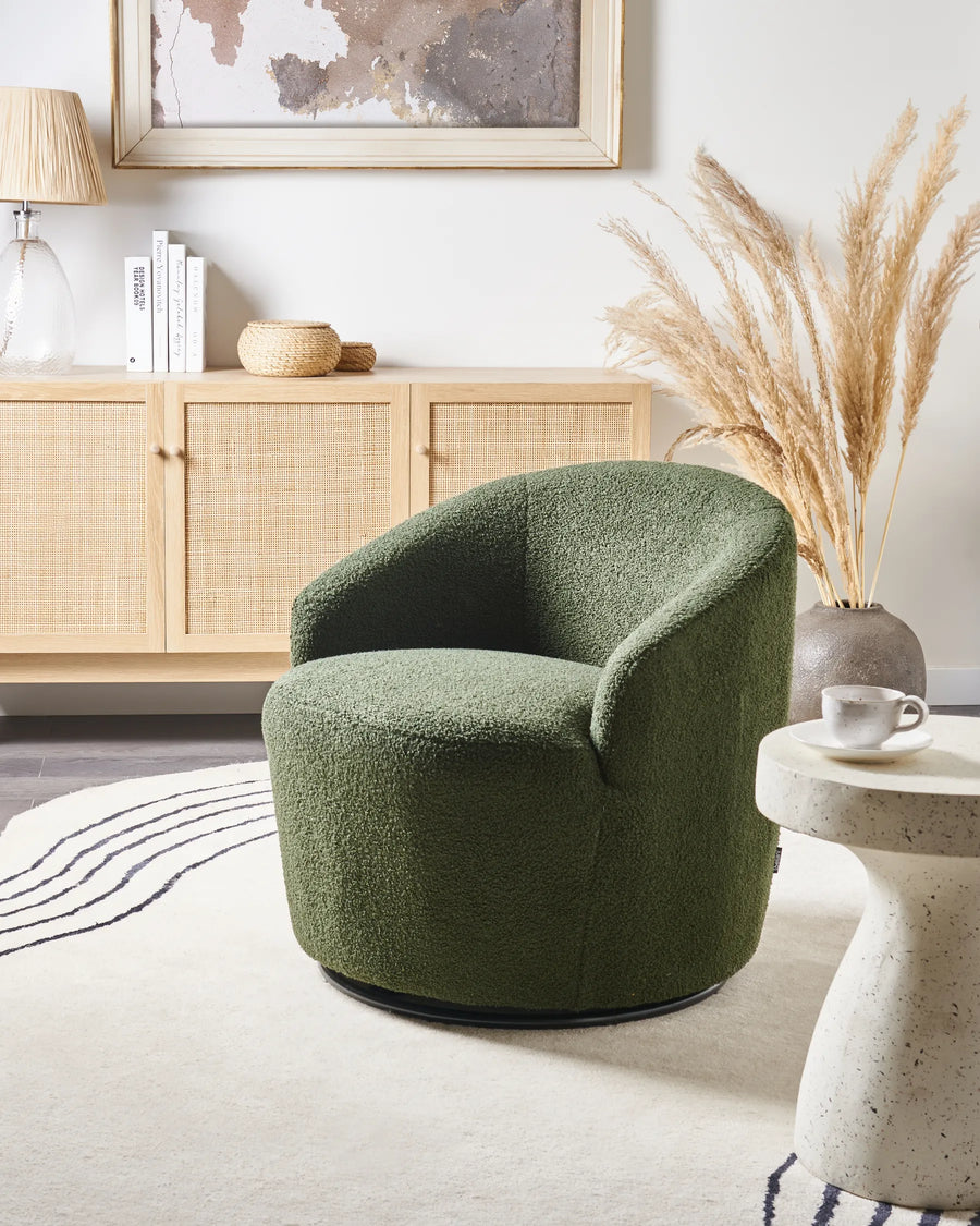Green armchair in a living room with a wooden sideboard and decorative elements.