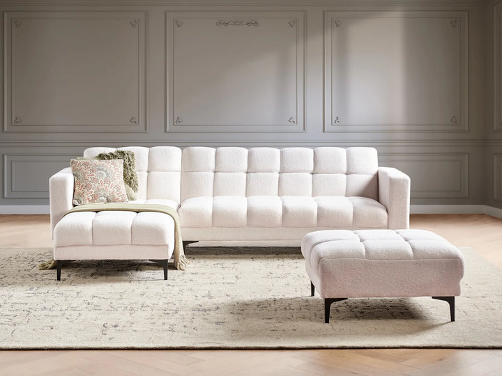 White sectional sofa with ottoman in a room with gray walls and wooden flooring.
