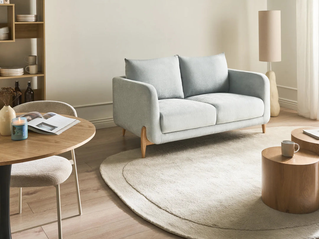Modern living room with a light gray sofa, wooden coffee table, and round rug.