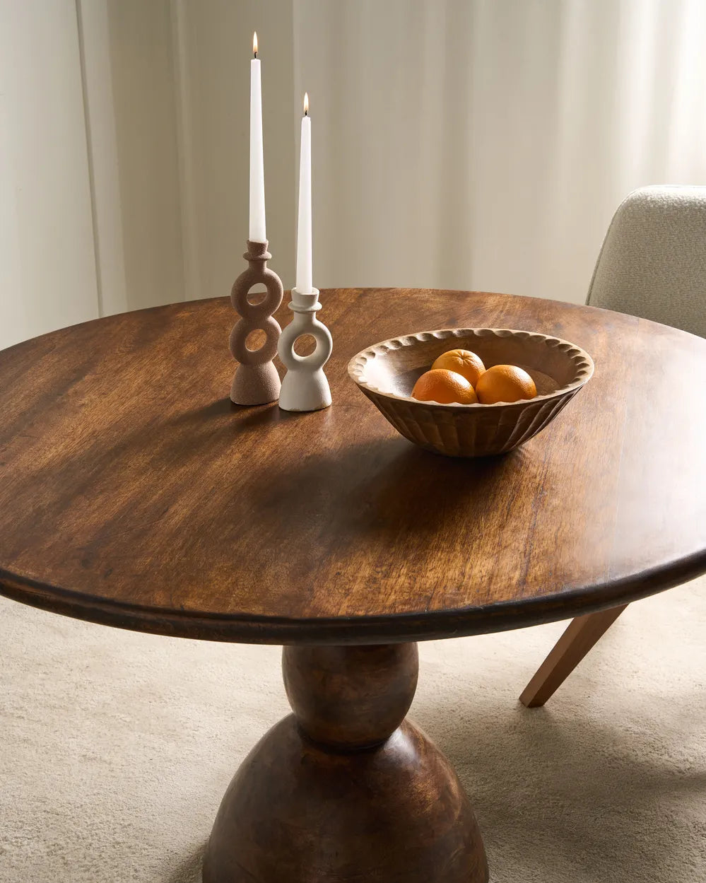 Wooden dining table with a bowl of oranges and candlesticks in a room.