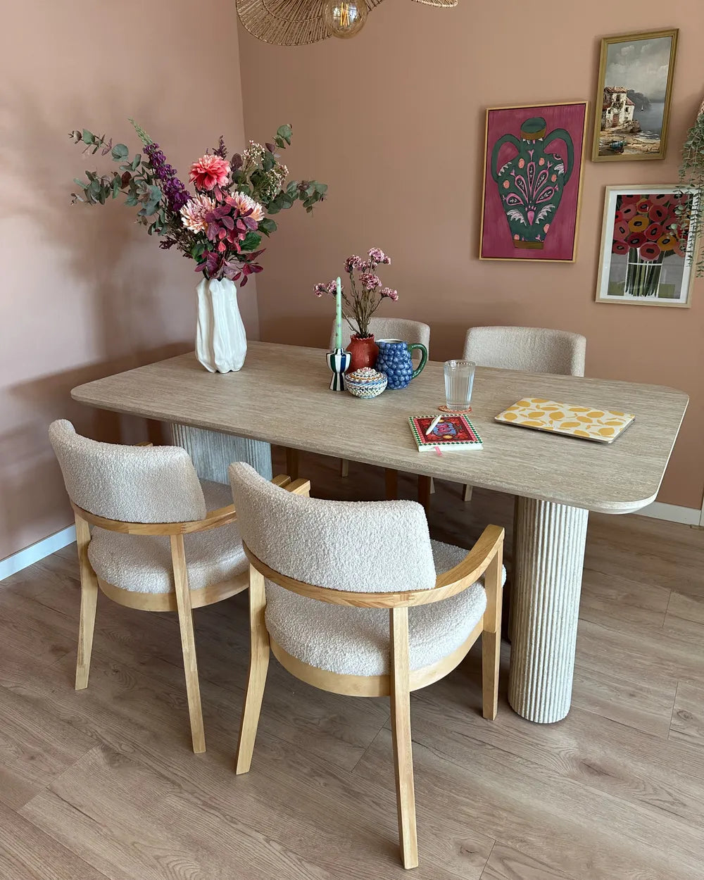 Dining area with a wooden table and chairs against a pink wall with decorative elements.
