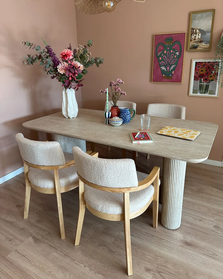 Dining area with a wooden table and chairs against a pink wall with decorative elements.