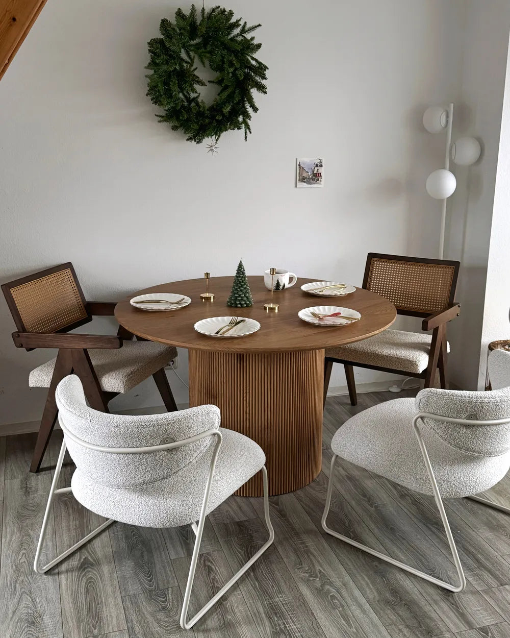Dining room with a round wooden table and chairs, including a wreath on the wall.