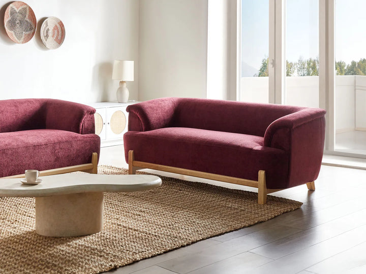 Maroon sofa and armchair set in a modern living room with a coffee table and decorative items.