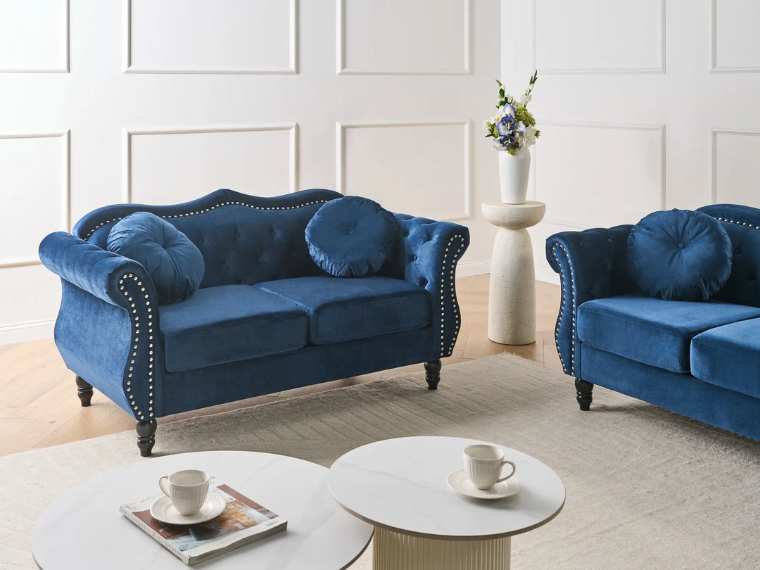Two blue velvet sofas in a living room setting with a white wall and coffee table.