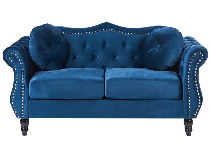 Blue velvet sofa with tufted backrest and nailhead trim on a white background
