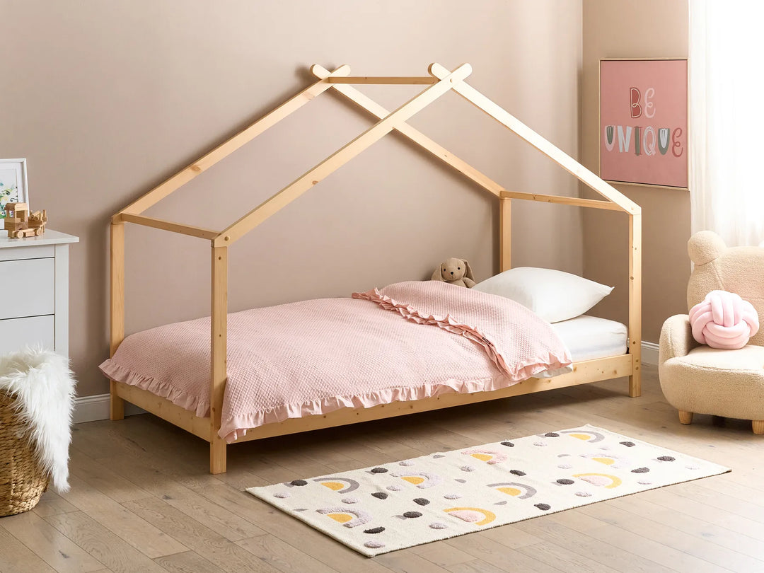 Children's room with a wooden house-shaped bed, pink bedding, and decorative elements.