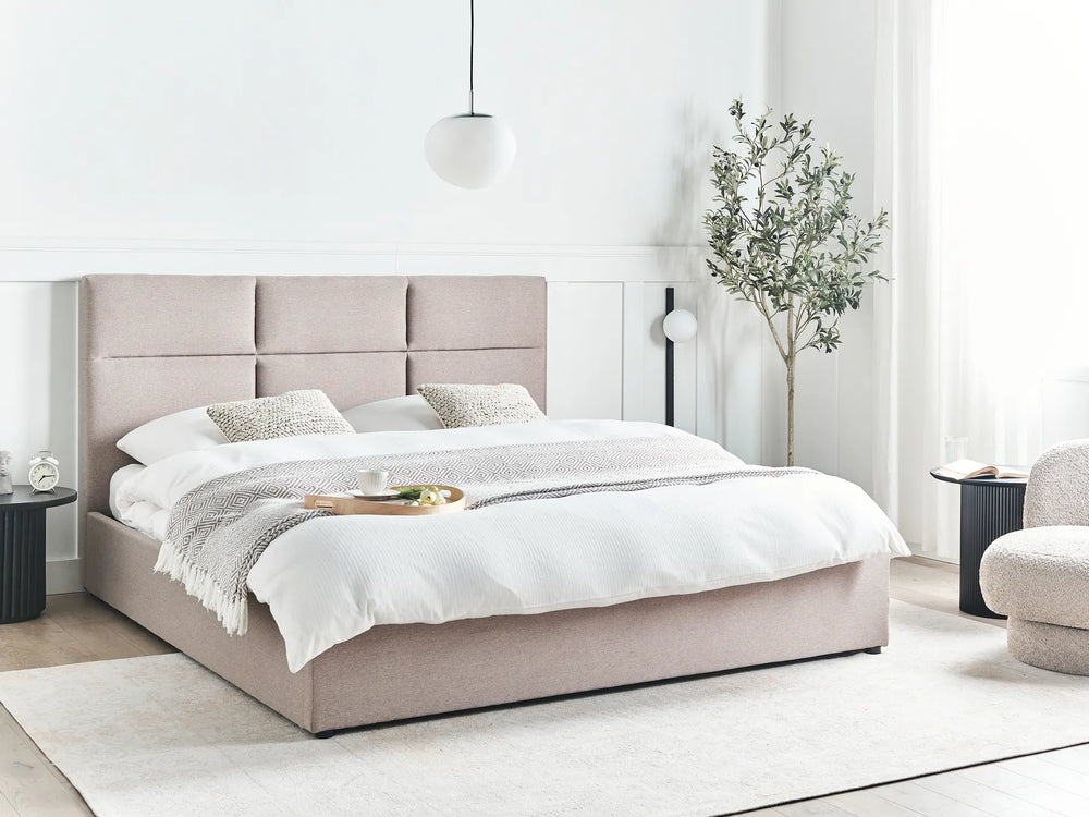 Beige upholstered bed in a modern bedroom setting with white walls and minimal decor.