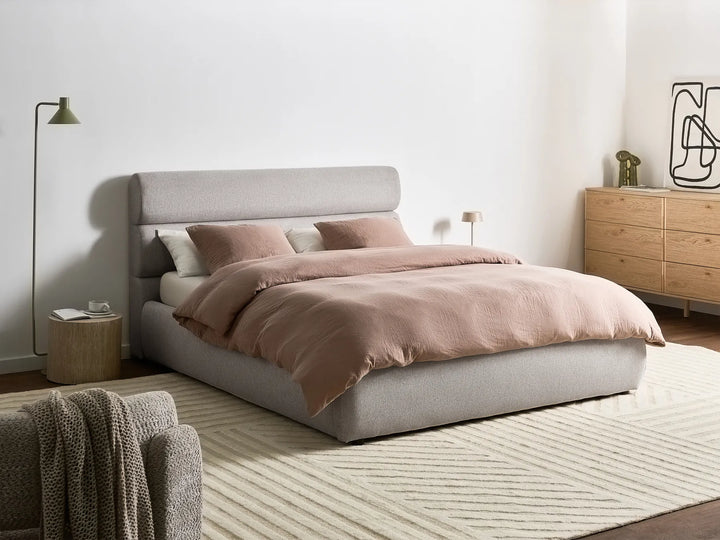 Modern bedroom with a gray upholstered bed, pink bedding, and wooden dresser.
