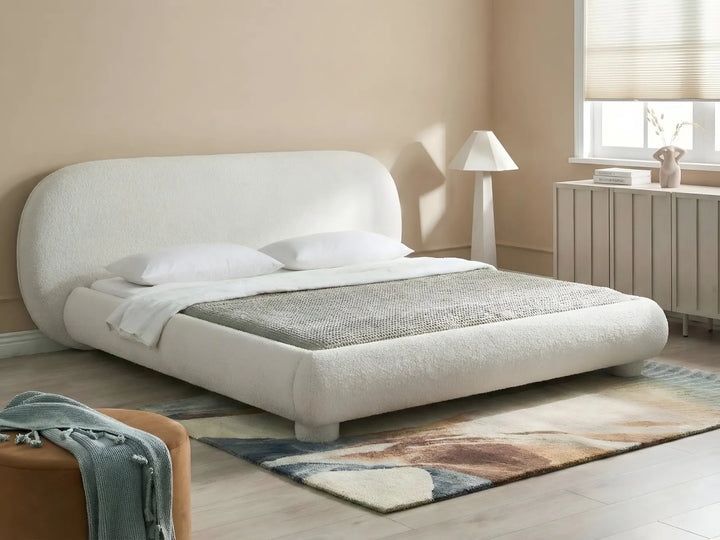 Modern bedroom with a white upholstered bed, lamp, and rug.