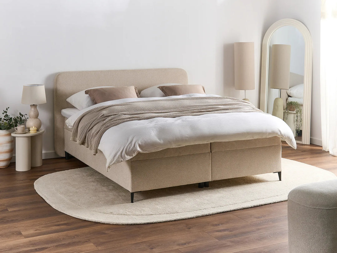 Beige upholstered bed in a bedroom setting with lamps and decor.