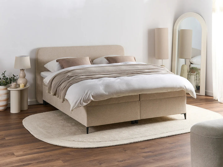 Beige upholstered bed in a bedroom setting with lamps and decor.