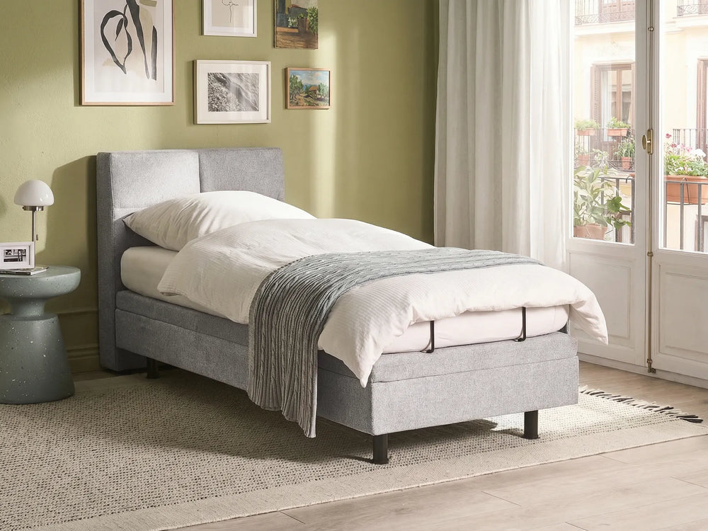 Gray upholstered bed in a room with green walls and a window.