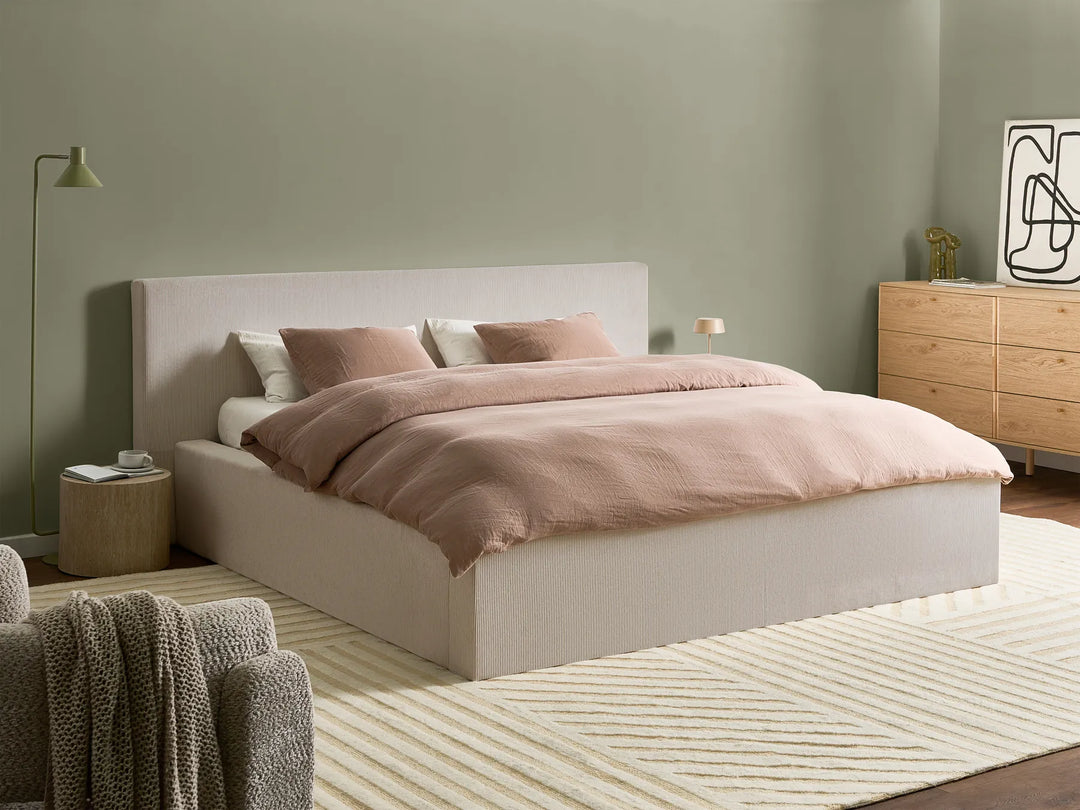 Neatly made bed with pink bedding in a bedroom setting.