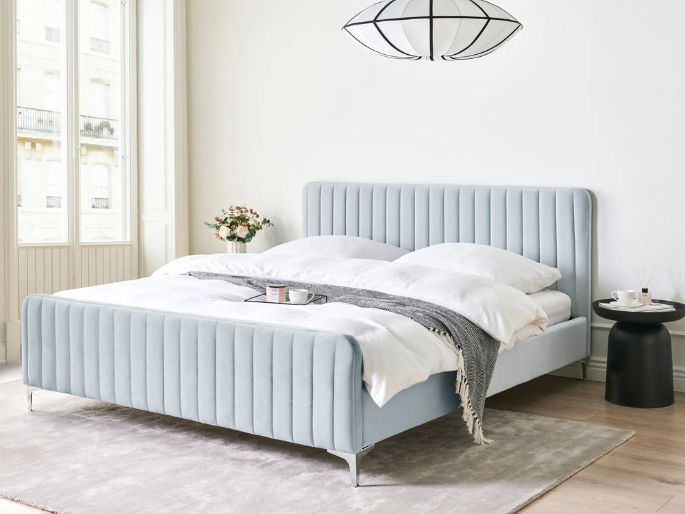Light blue upholstered bed in a room with large windows and a rug.