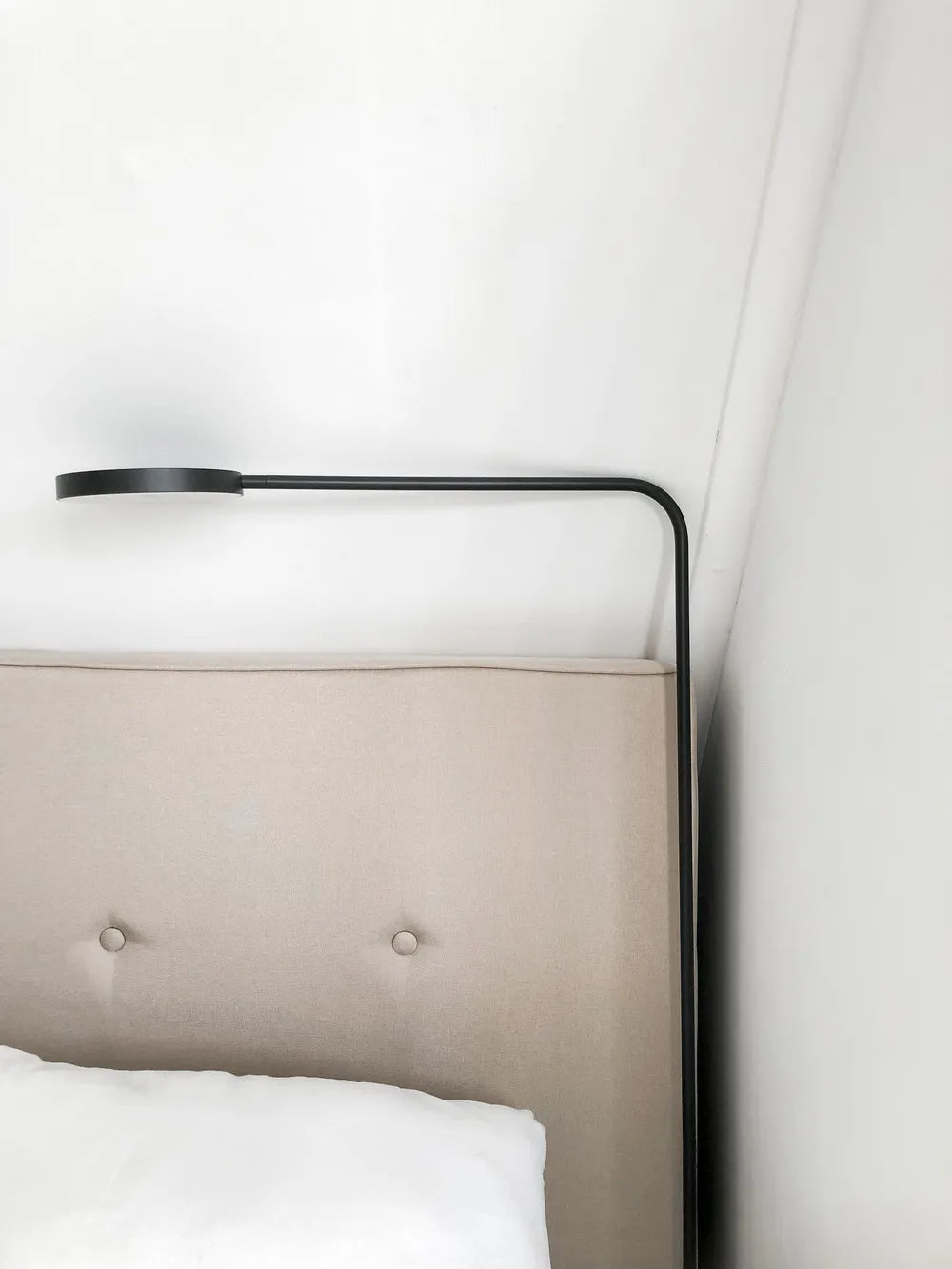 Modern bed with beige upholstered headboard and black metal frame against a white wall.