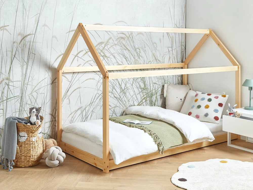 Wooden house-shaped bed in a child's bedroom with decorative pillows and toys.