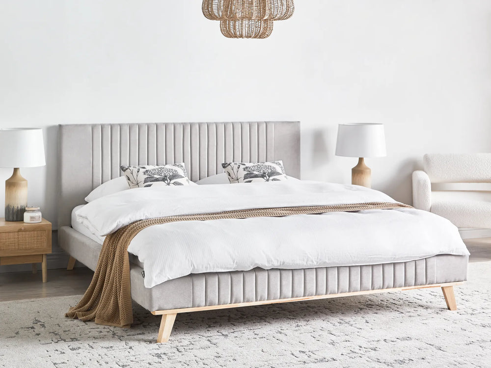 Neatly made bed with white bedding and a gray headboard in a bright bedroom.