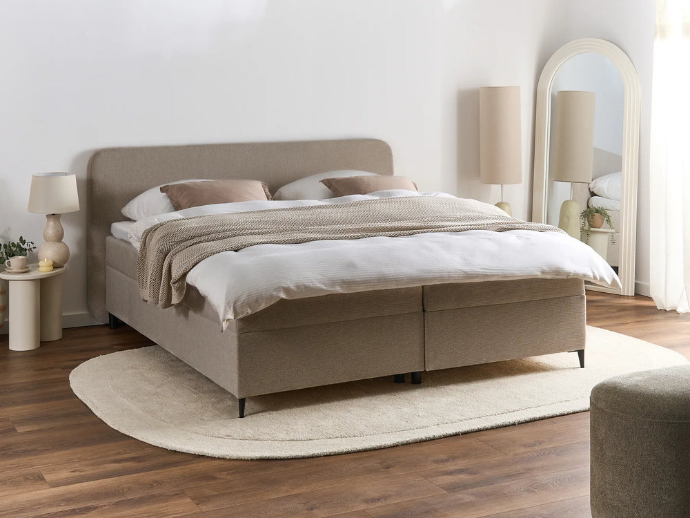 Beige upholstered bed in a bedroom setting with lamps and a mirror.