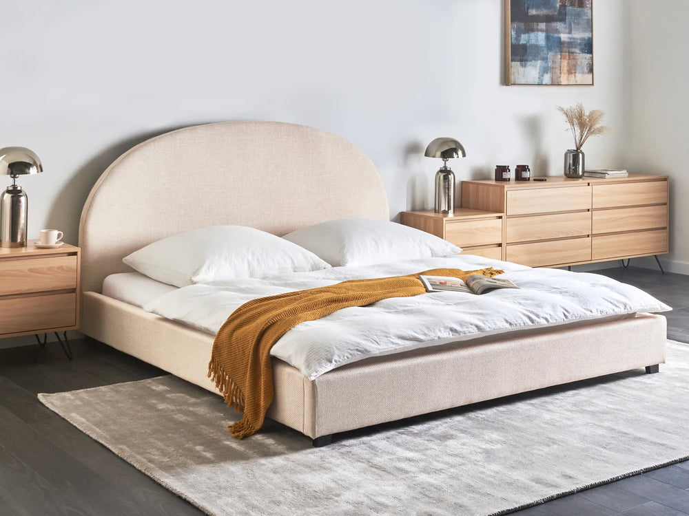 Beige upholstered bed with white bedding and a brown throw blanket in a bedroom setting.