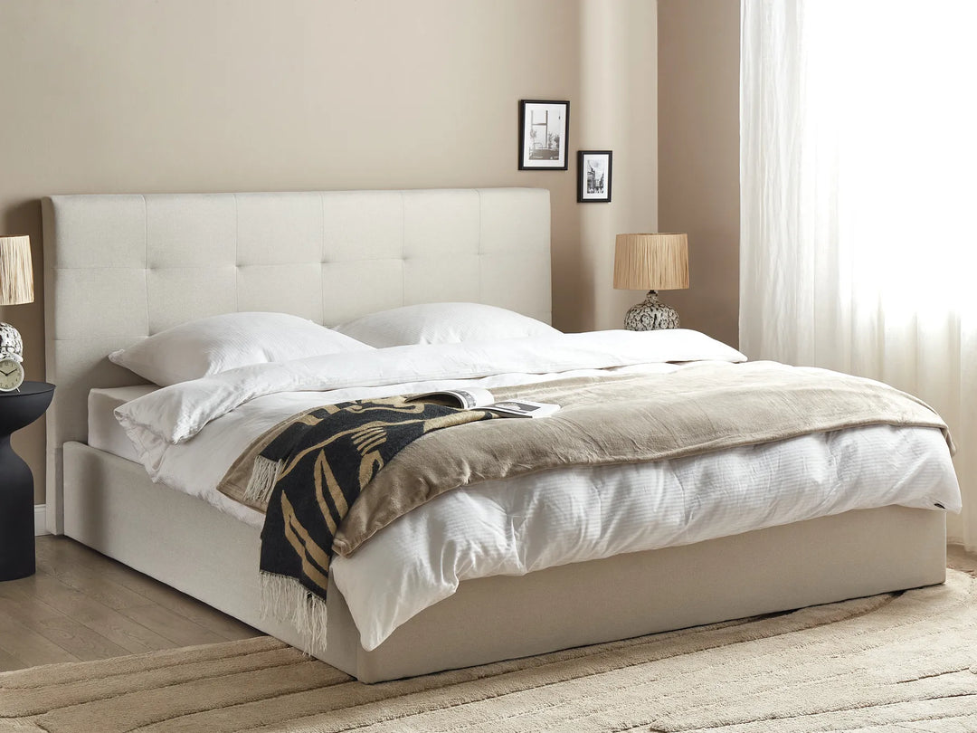 Beige upholstered bed with white bedding and a decorative blanket in a bedroom setting.