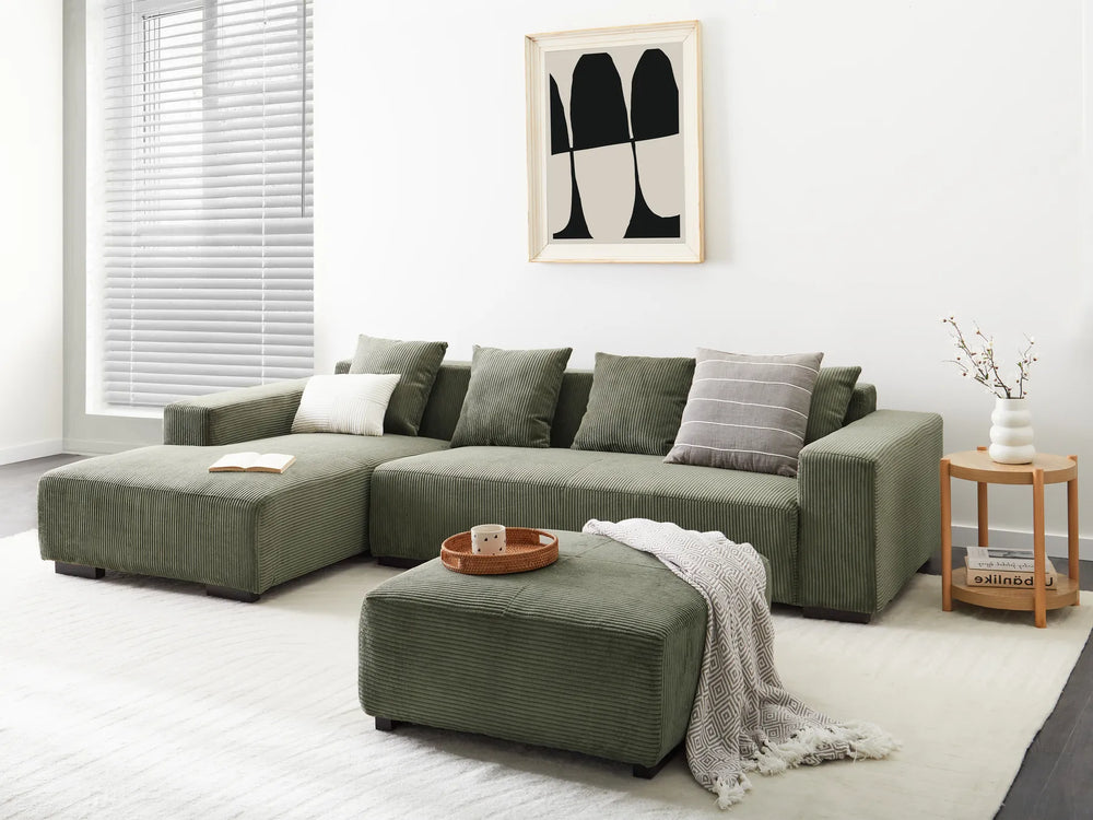 Green sectional sofa in a living room with a white wall and framed artwork.
