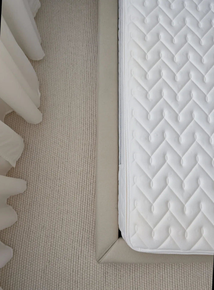 Close-up of a mattress corner with quilted design on a beige carpet