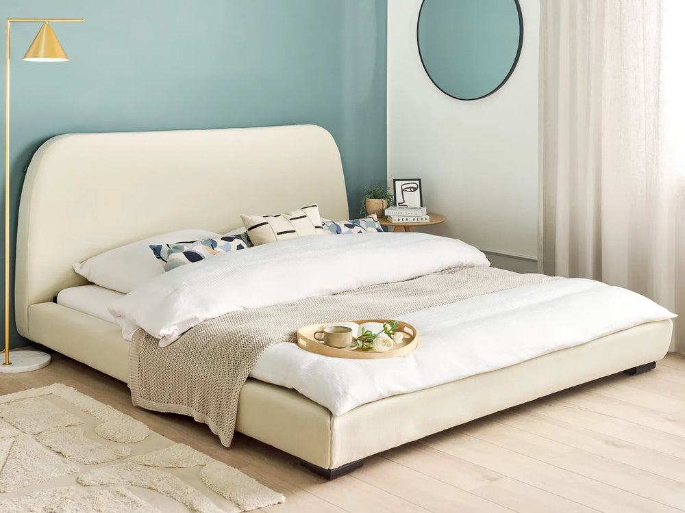 Beige upholstered bed in a room with a light blue wall and white curtains.