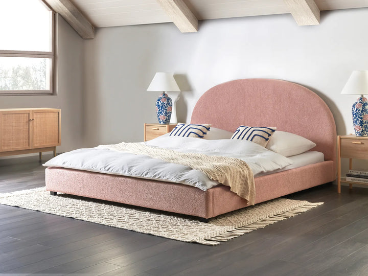 Pink upholstered bed in a room with wooden flooring and a window.
