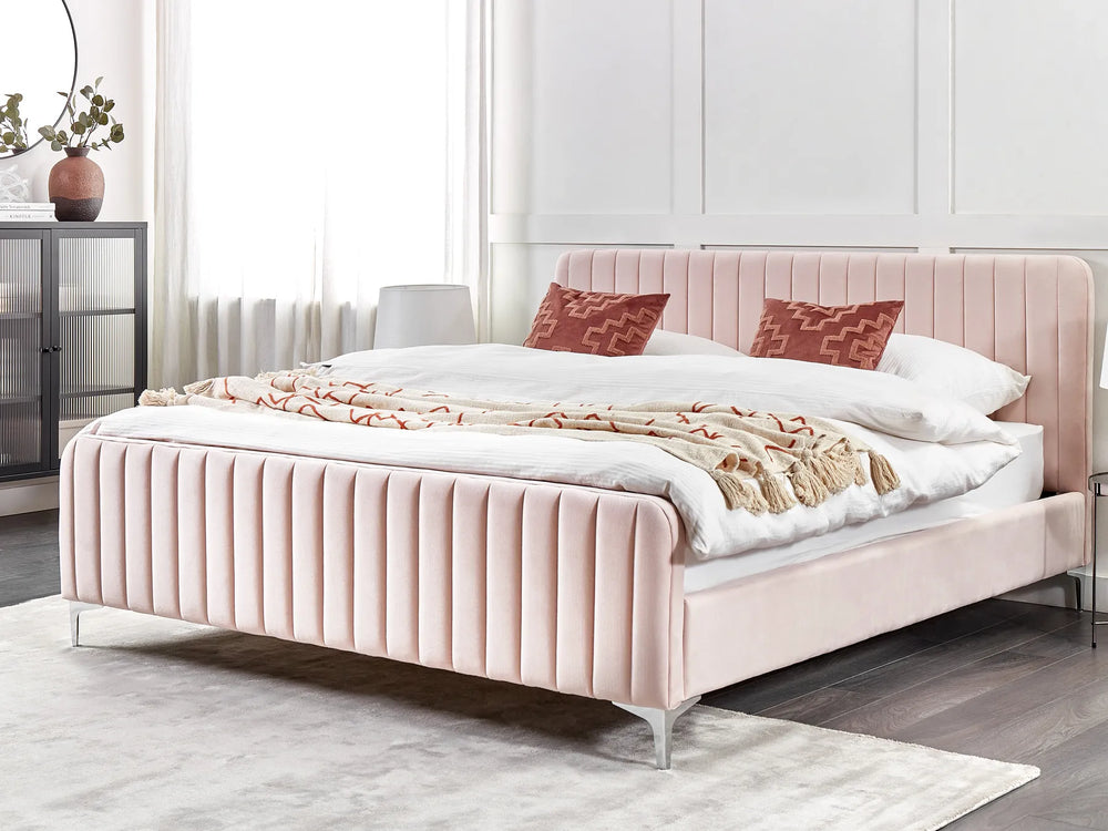 Pink upholstered bed with white bedding and red pillows in a bedroom setting.