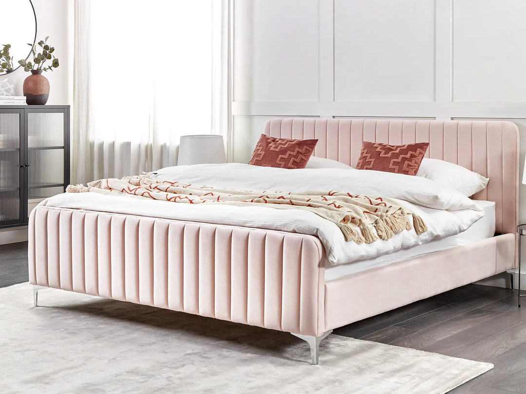 Pink upholstered bed with white bedding and red pillows in a bedroom setting.