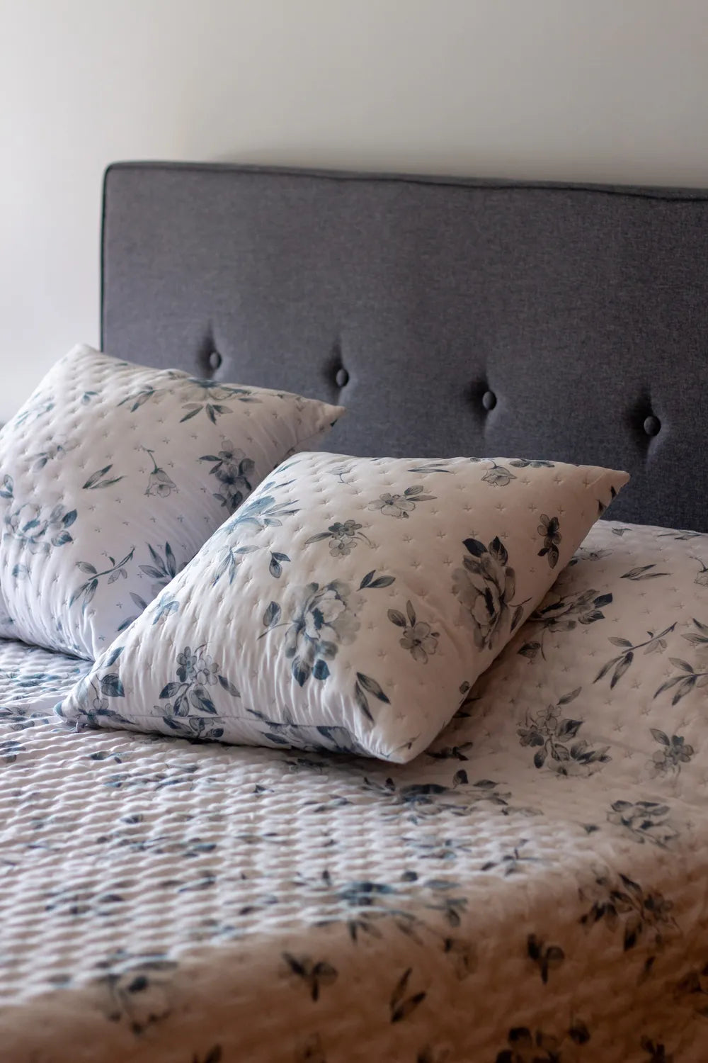 Floral-patterned pillows on a bed with a tufted headboard.