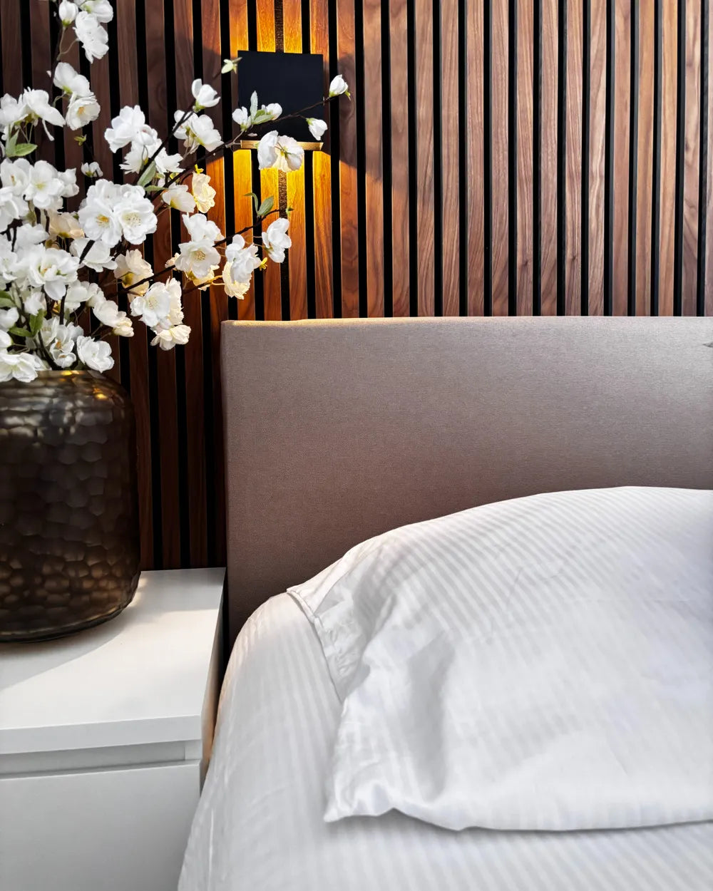 Bedroom with a bed, white flowers in a vase, and wooden wall.