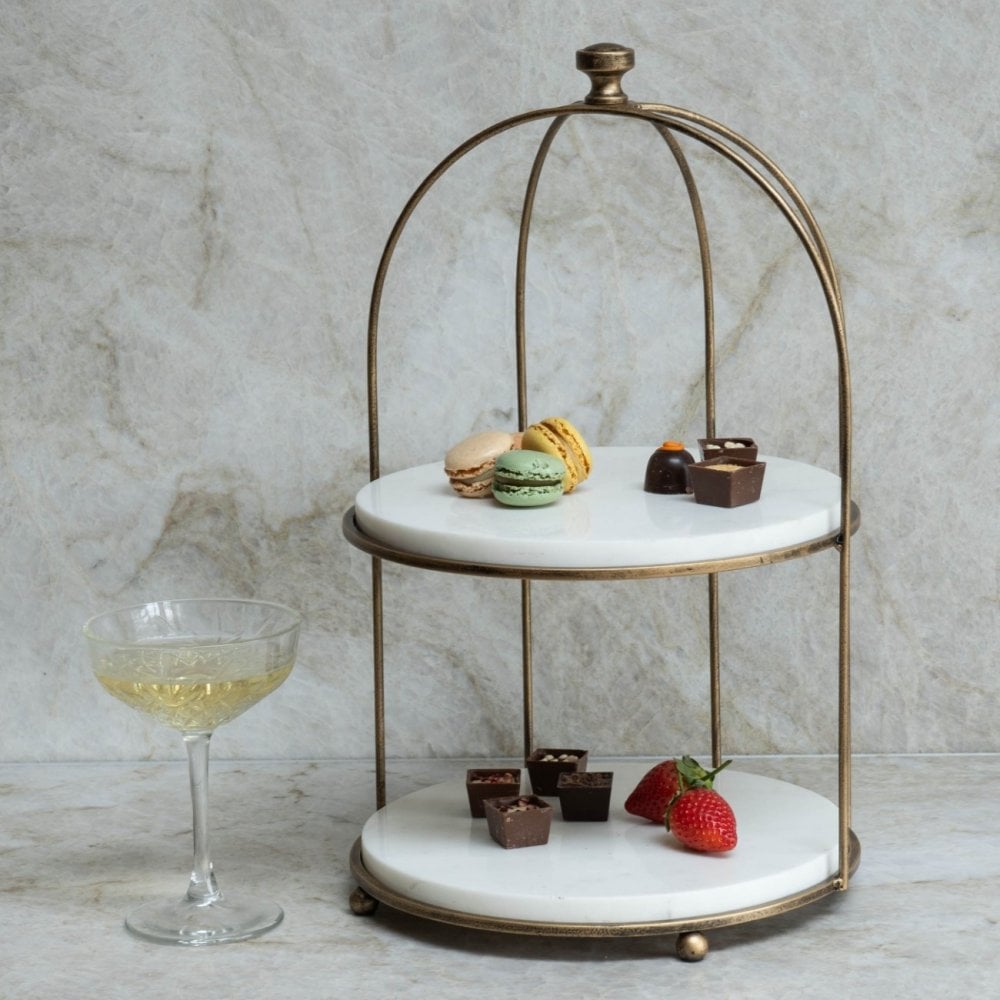 Two-tiered marble dessert stand with pastries and a glass of white wine on a marble surface.