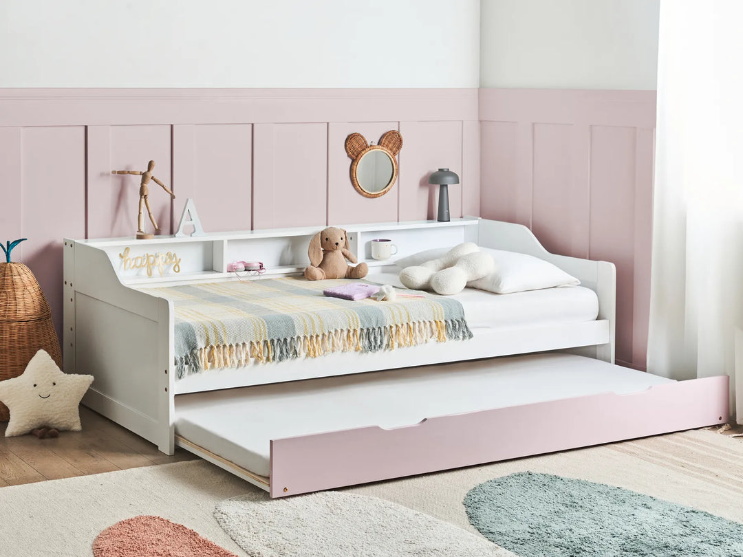 Children's bed with a white frame and pink storage drawer in a room with pink walls and wooden floor.