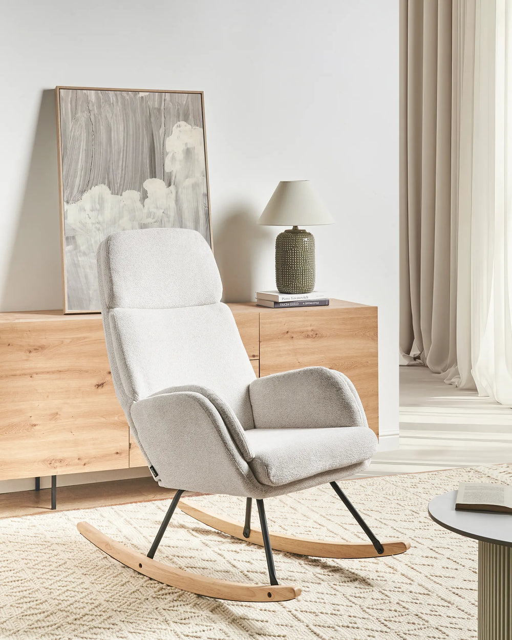 White rocking chair in a room with wooden dresser and lamp