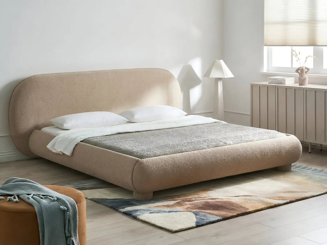 Beige upholstered bed in a modern bedroom with a lamp and window.