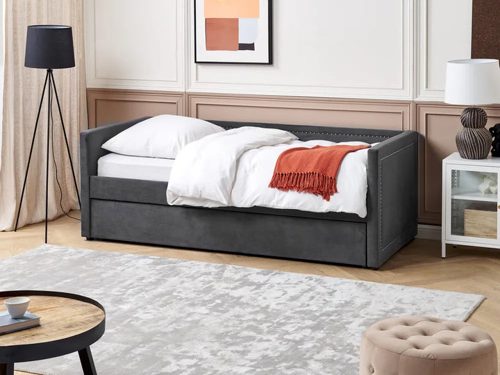 Gray upholstered bed with white bedding and a red blanket in a bedroom setting.