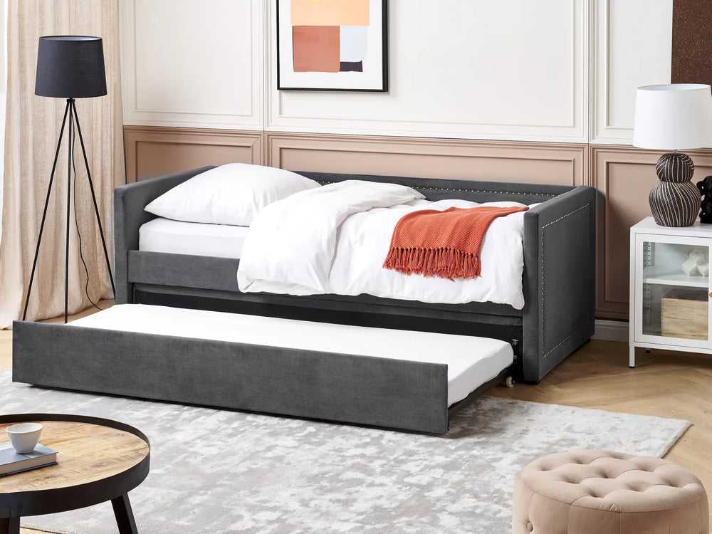 Gray upholstered bed with white bedding and a red blanket in a bedroom setting.
