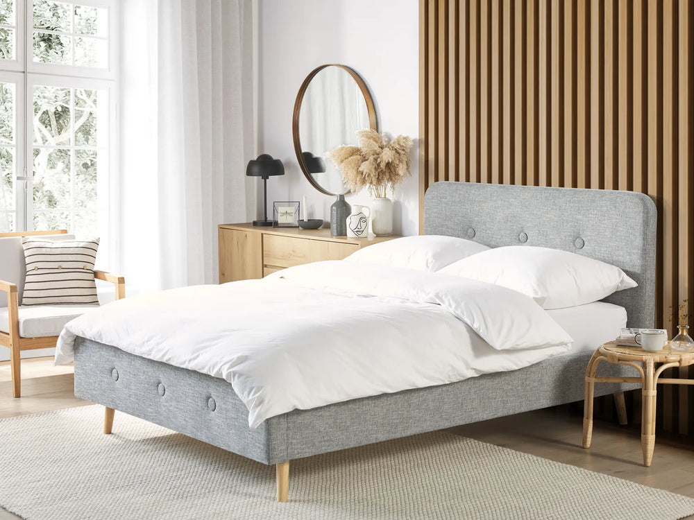 Gray upholstered bed in a bedroom with white bedding and wooden furniture.