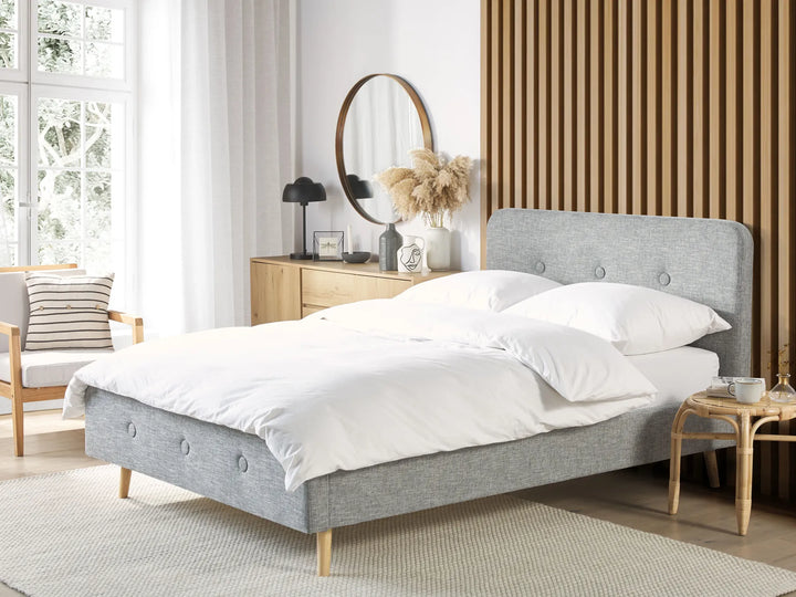 Gray upholstered bed in a bedroom with white bedding and wooden furniture.