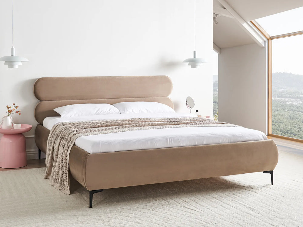 Beige upholstered bed in a modern bedroom with large windows.