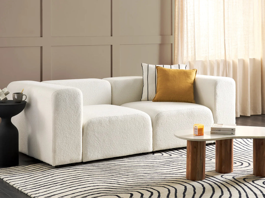 Modern living room with a white sofa, gold pillow, and wooden coffee table.