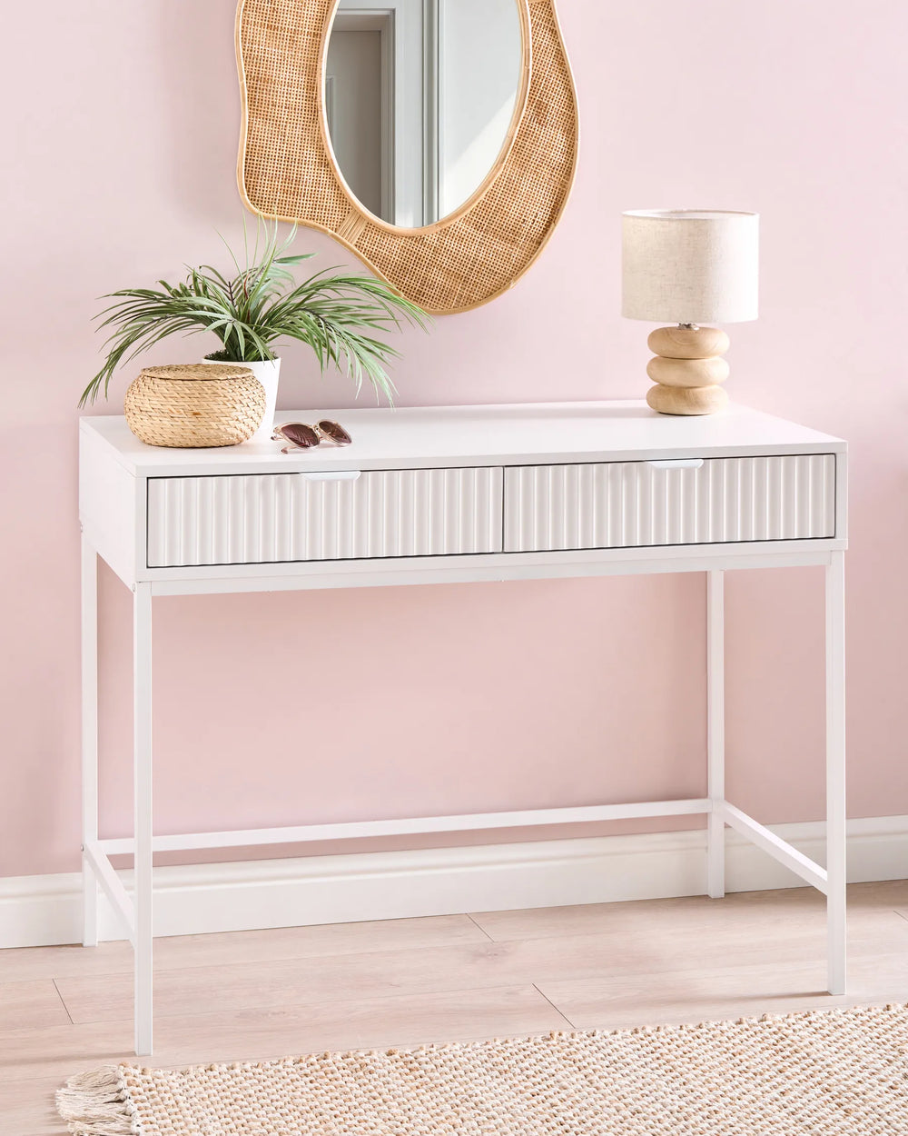 White console table with decorative items against a pink wall