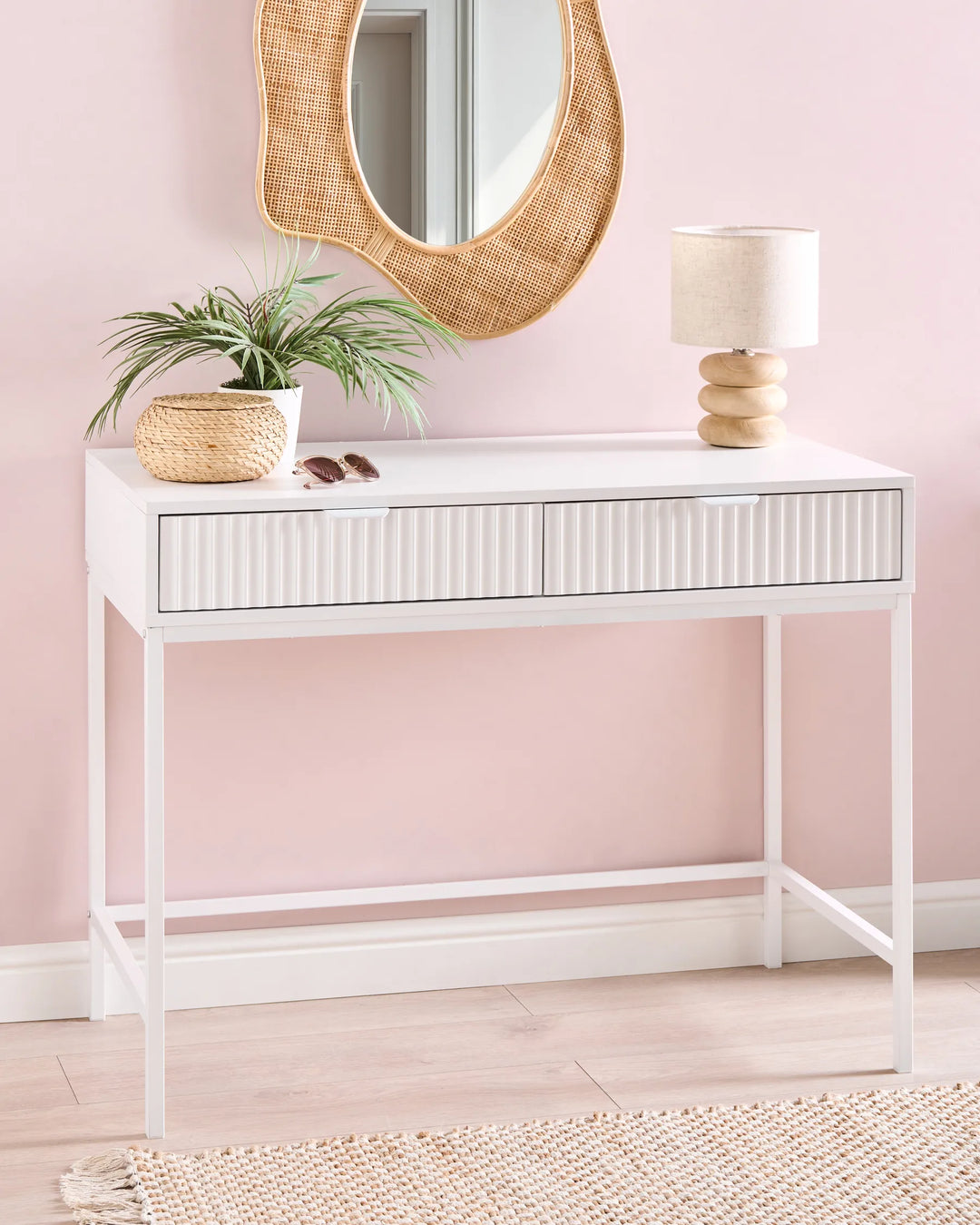 White console table with decorative items against a pink wall