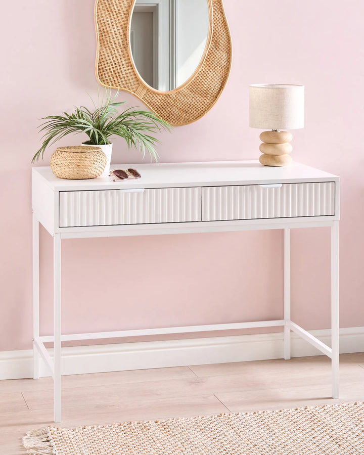 White console table with decorative items against a pink wall