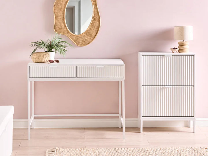 White console table and cabinet against a pink wall with decorative items.
