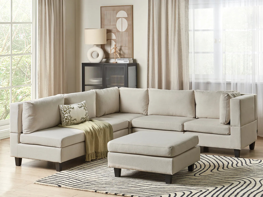 Beige sectional sofa in a living room with a striped rug and window curtains.