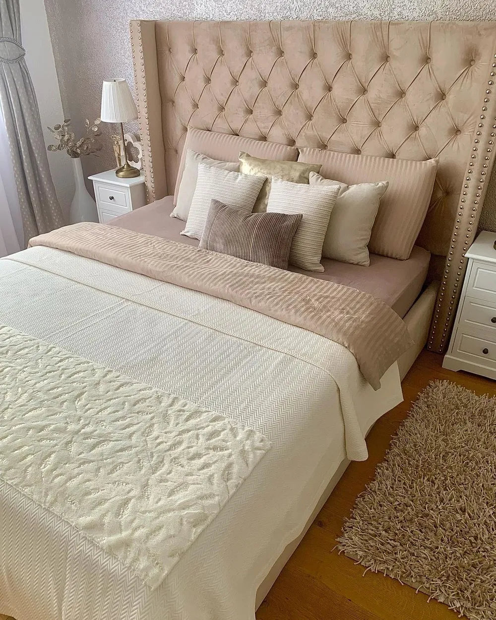 Neatly made bed with decorative pillows and a textured headboard in a bedroom setting.