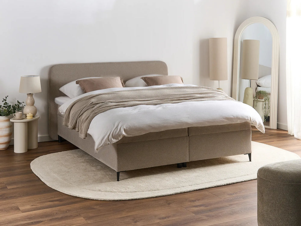 Beige upholstered bed in a bedroom setting with lamps and decor.
